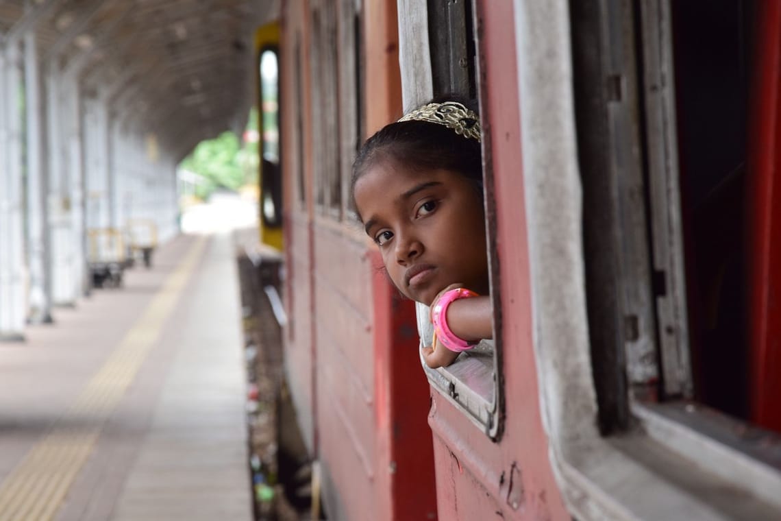 A little girl peaking out the window of a train waiting at the station