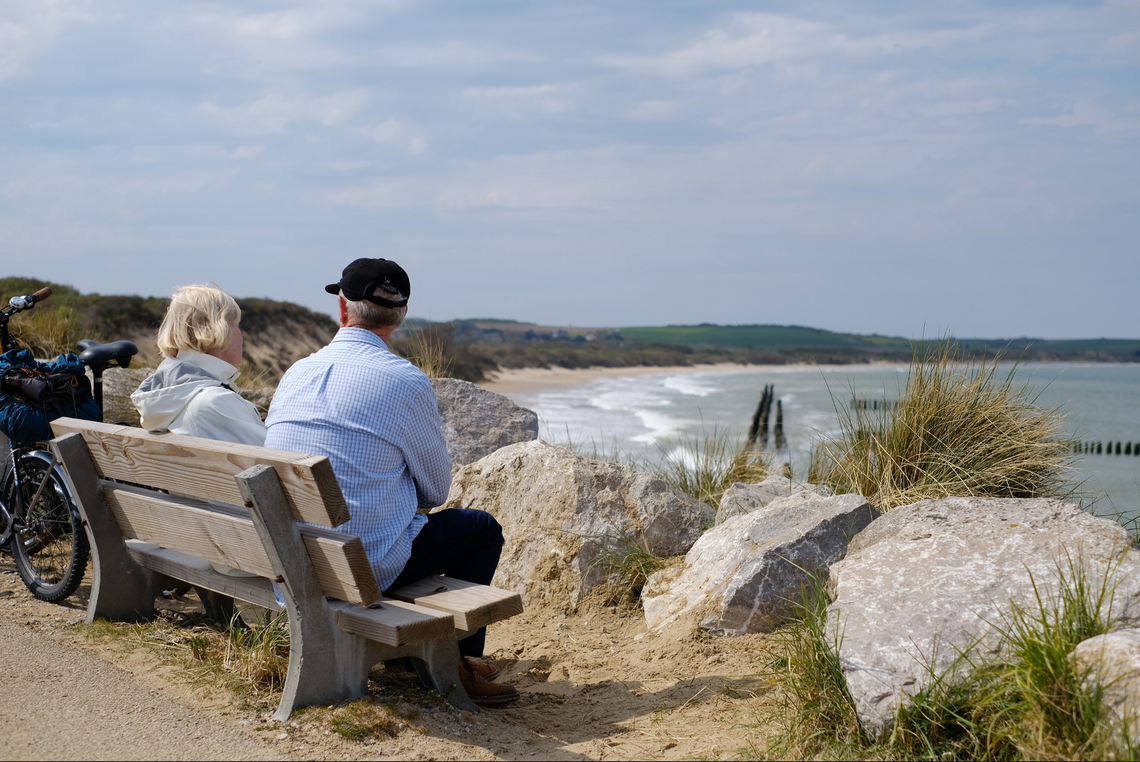 A couple resting on a bench by a cliff overlooking the sea