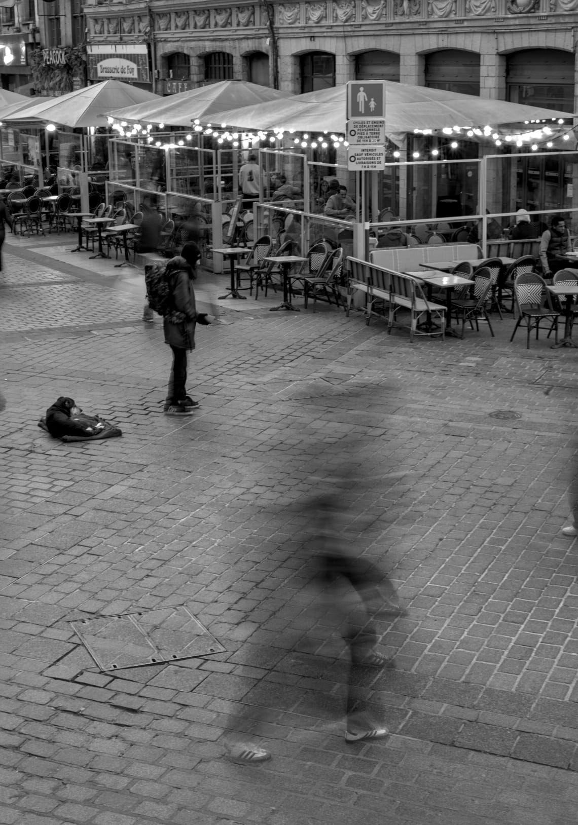 Black and white picture depicting a homeless person waiting with his hand open while the passages of people are blurred around him