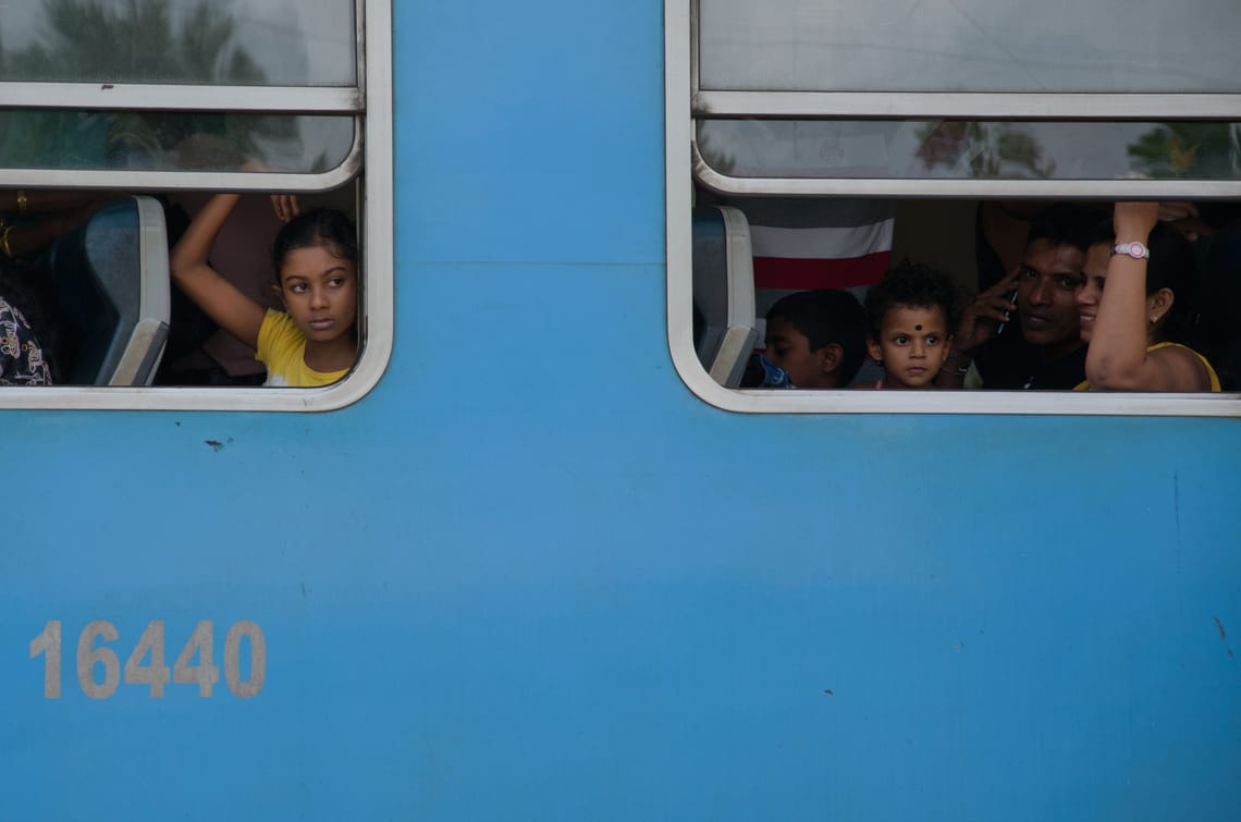 Kids looking out a blue train's windows, waiting to depart